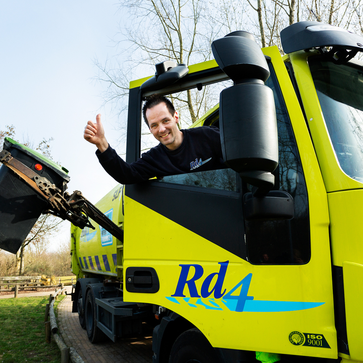 Een lachende inzamelmedewerker steekt zijn duim op vanuit een Rd4 wagen, terwijl hij een GFT-container leegt.